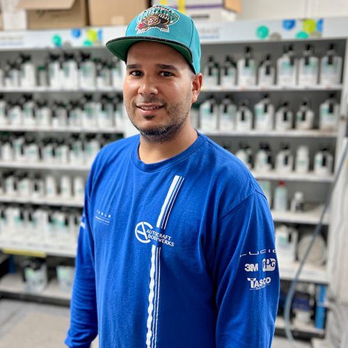 Man in blue shirt and teal cap smiles in front of paint shelves.