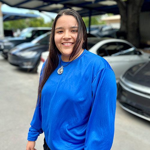 Person in a blue shirt smiles in front of cars.