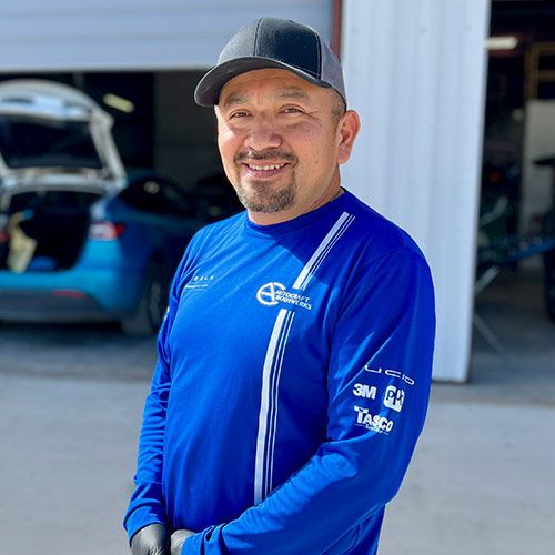 Man in blue shirt and baseball cap smiles in front of a garage.