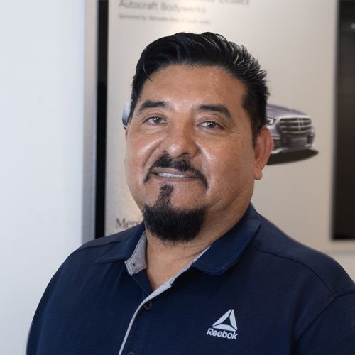 Smiling man in a navy Reebok shirt standing indoors near an automotive poster