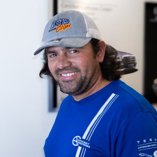 Smiling man in a gray cap and blue shirt standing indoors against a light wall