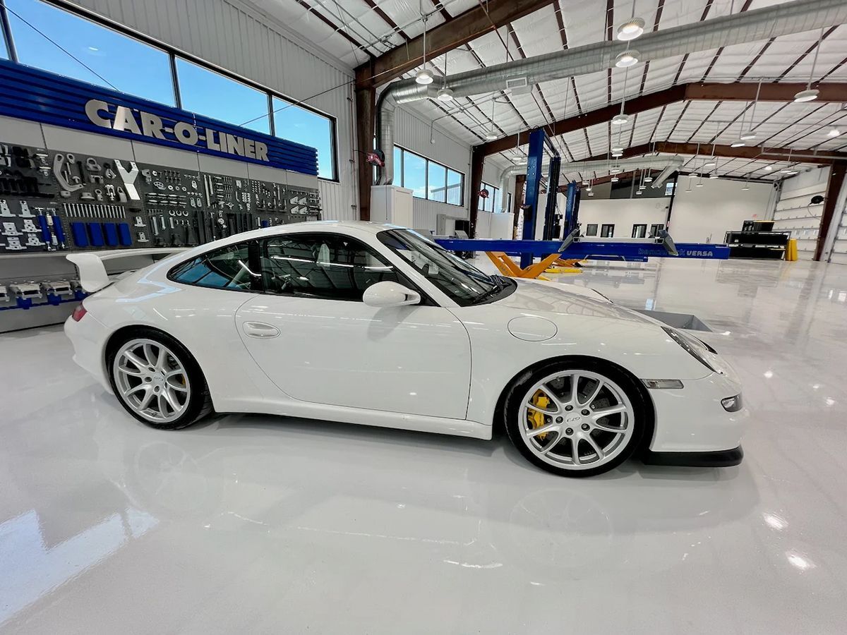 White Porsche sports car in a modern auto shop, with yellow brake calipers and shiny floor.