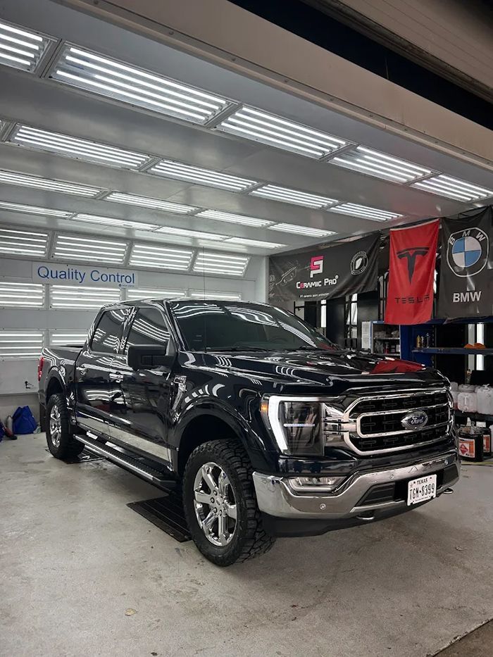 Black Ford F-150 truck in a brightly lit garage, parked in front of banners.