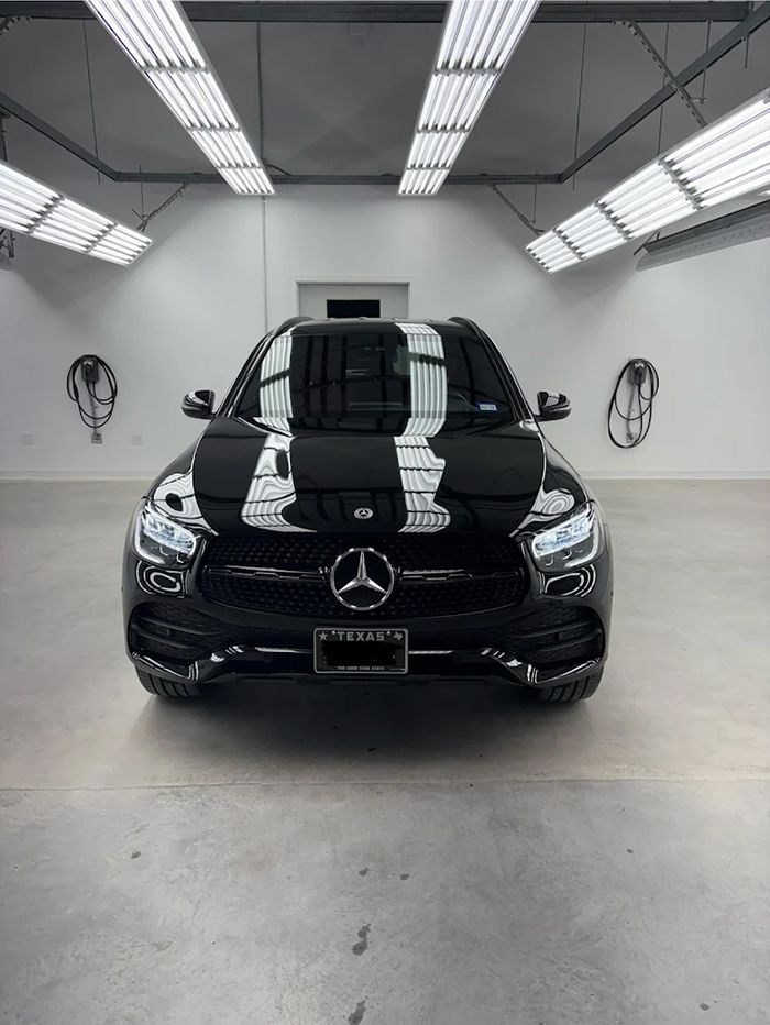 Black Mercedes SUV in a bright, white-walled garage under overhead lights.