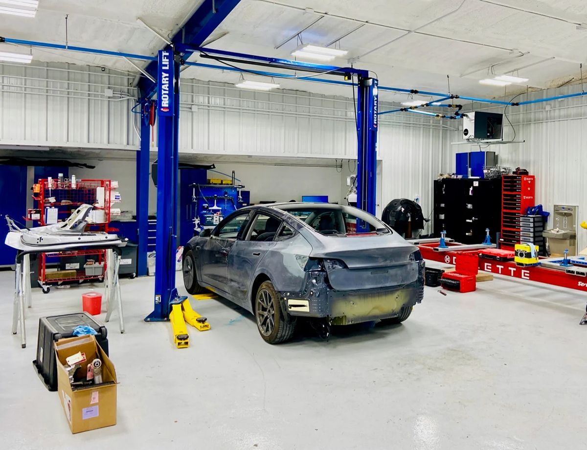 A car undergoing repair in an auto shop, with a lift, tools, and a damaged rear end.