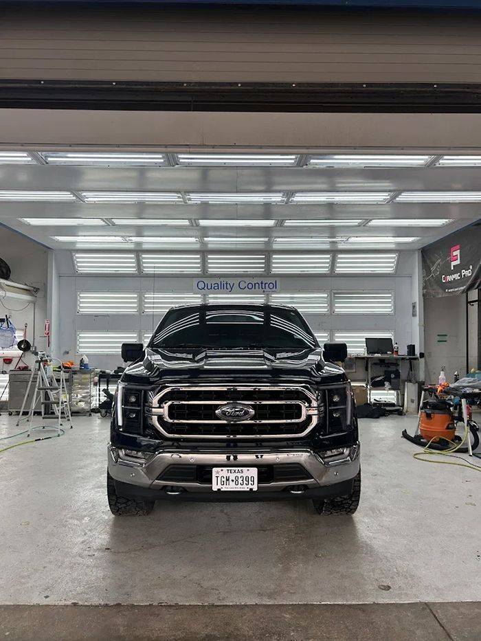 Black Ford truck in a garage; front view. Silver grill, license plate, and bright lighting.