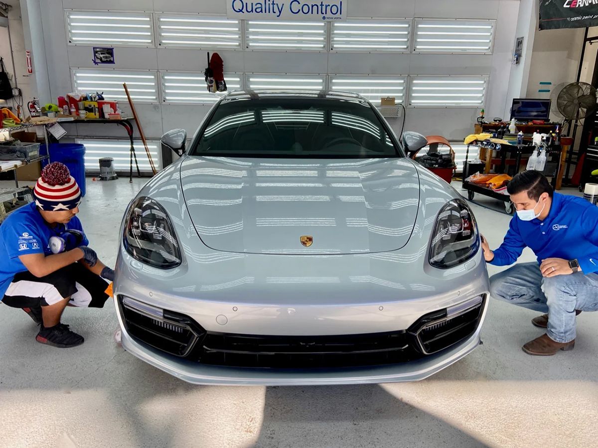 Two men inspecting a silver Porsche in a well-lit auto shop; 