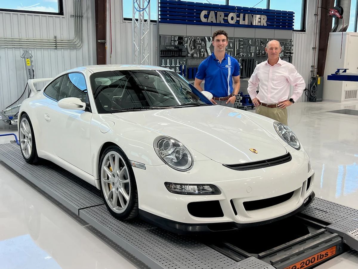 A white Porsche on a lift with two men in a workshop.