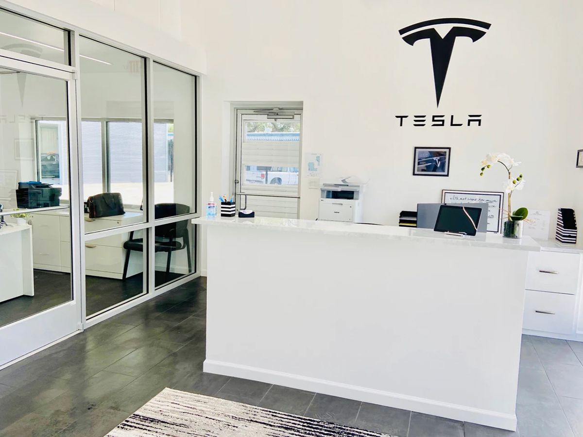 Tesla service center reception area with white walls, desk, and logo.