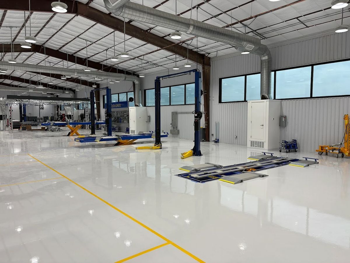 Brightly lit auto repair shop with vehicle lifts and equipment. White floor and walls, metal ceiling.