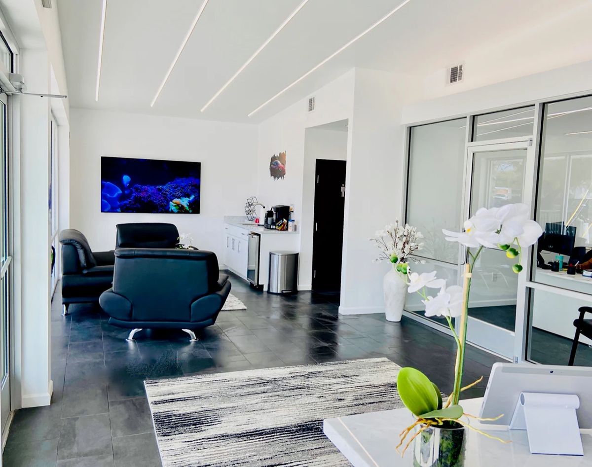 Modern office reception area with black leather chairs, white walls, and a large TV.