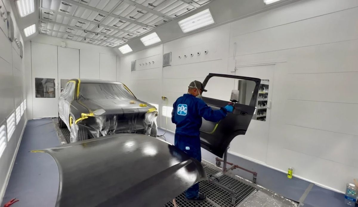 A person painting a car door inside a car painting booth.