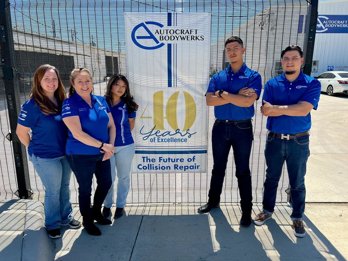 Group of people in blue shirts stand in front of AutoCraft Bodyworks banner celebrating 10 years.