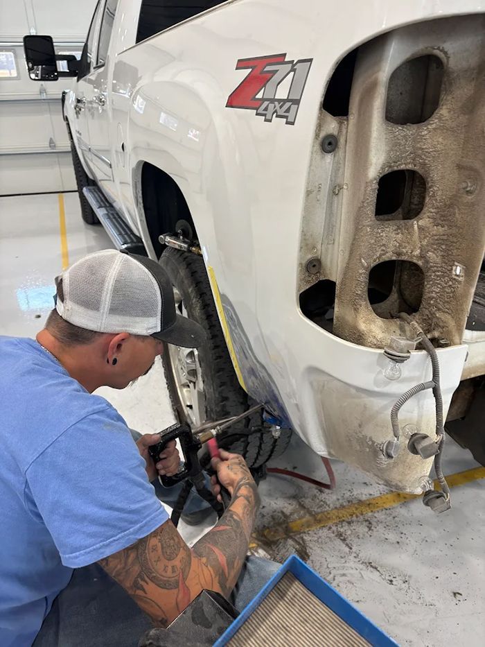 A person works on a white truck's damaged rear. The truck has Z71 badging. The setting is indoors.