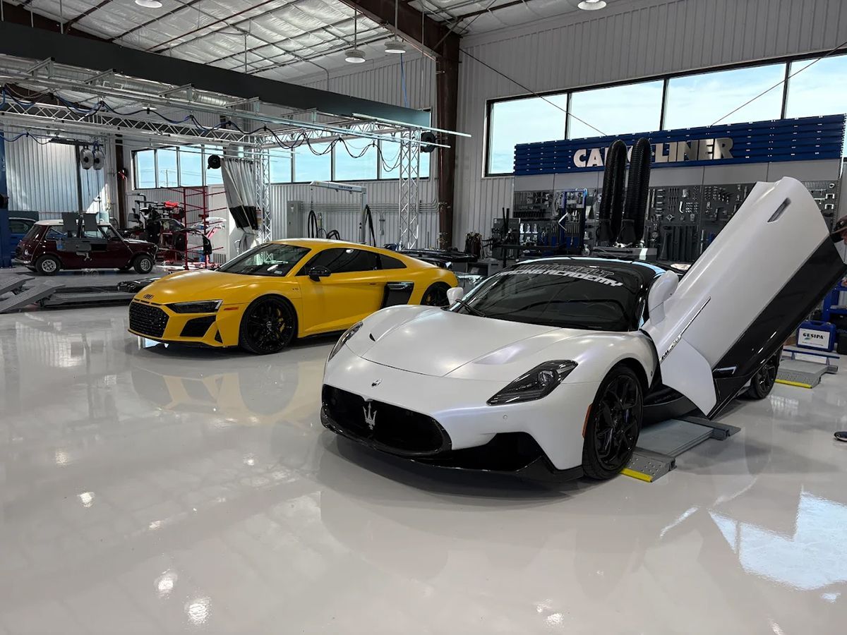 White sports car with open doors and yellow sports car inside a hangar.