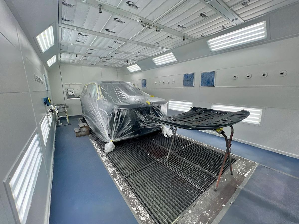 Car covered in plastic inside a professional paint booth, ready for painting.