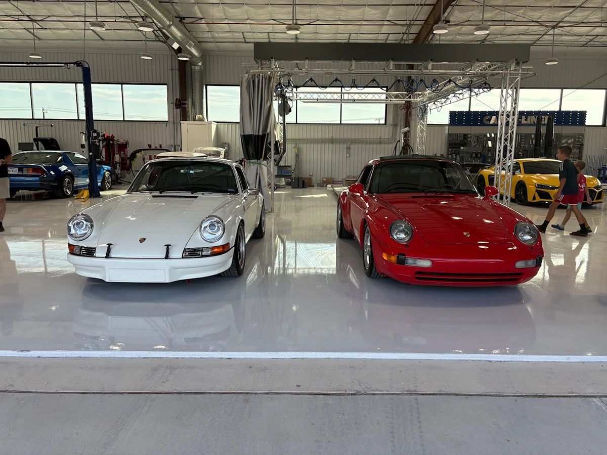 White and red Porsche sports cars parked in a brightly lit garage. People walk around.
