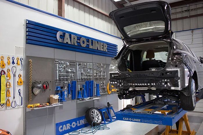 Car-O-Liner auto body shop. A car with its trunk open on a lift, tools on wall, and a spare tire nearby.