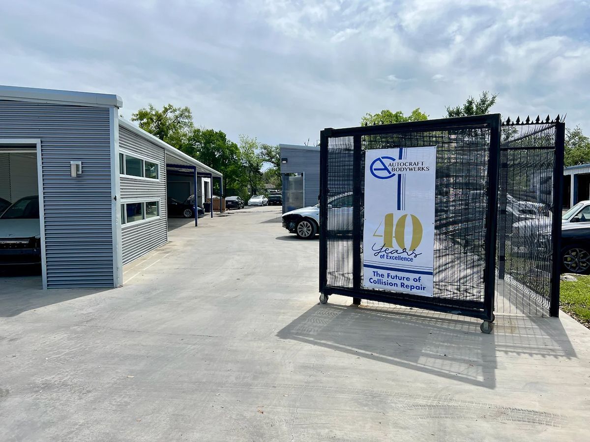 Gated car storage facility with a sign celebrating a 10th anniversary. Gray buildings and vehicles are visible.