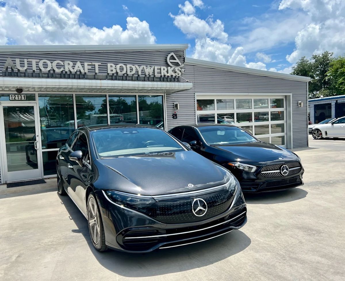Two Mercedes-Benz vehicles parked in front of Autocraft Bodywerks building with a clear blue sky.