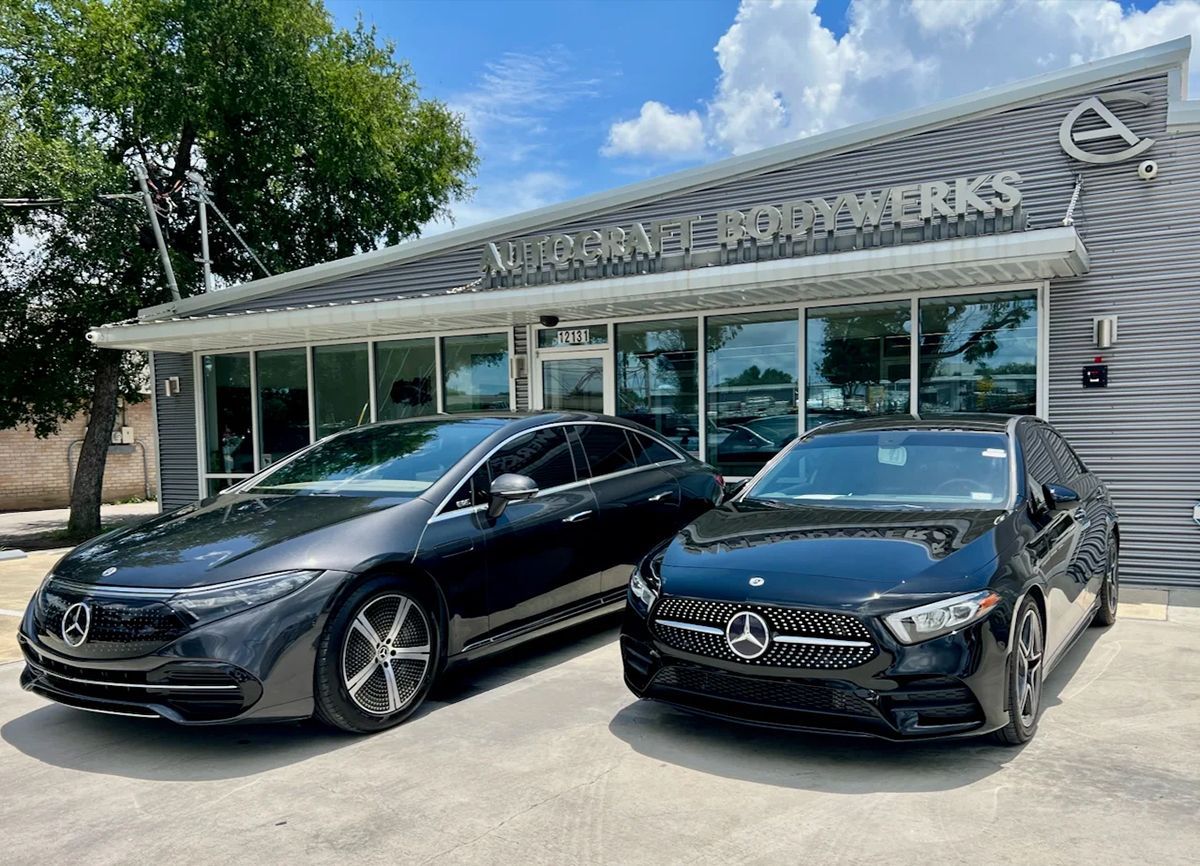 Two black Mercedes sedans parked in front of a Mercedes-Benz repair shop on a sunny day.