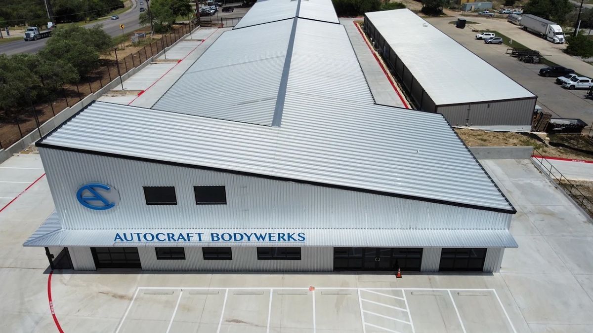 Exterior view of Autocraft Bodyworks building with angled roof and blue logo, surrounded by parking.