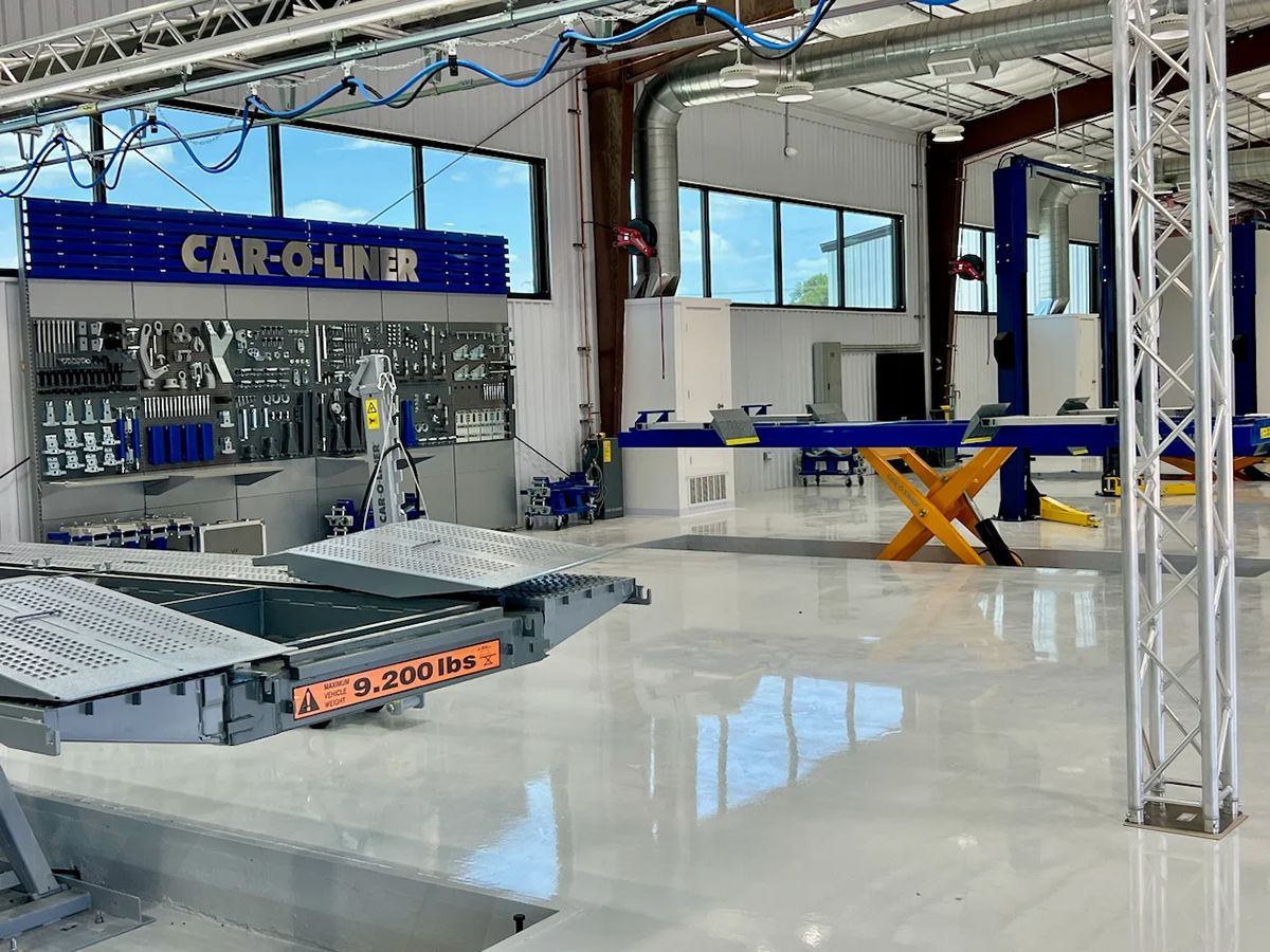 Inside an auto body shop, a car lift is in use near a Car-O-Liner repair station. Blue and white interior.