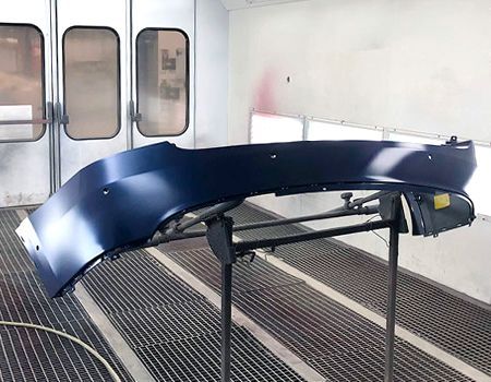 Dark blue car bumper in a paint booth, mounted on a stand.