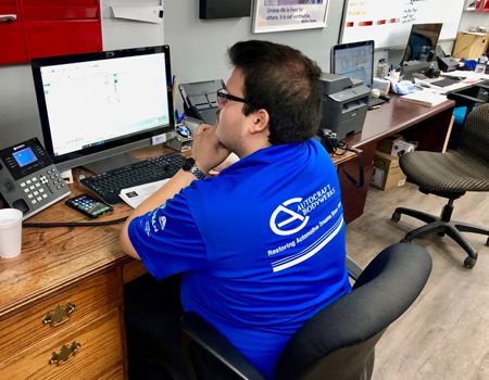 Man in blue shirt at desk, looking at computer screen, holding chin, office setting.