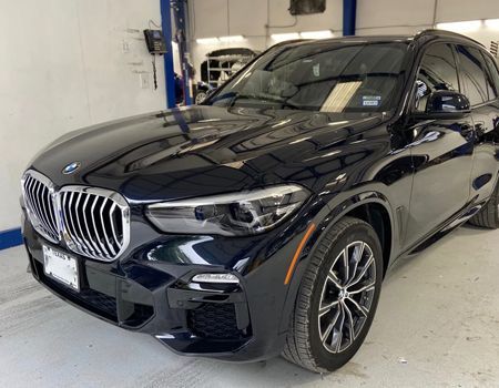Black BMW SUV parked indoors, shiny, front view, in a bright shop setting.