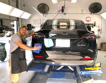 Man polishing a black Tesla car in a repair shop.