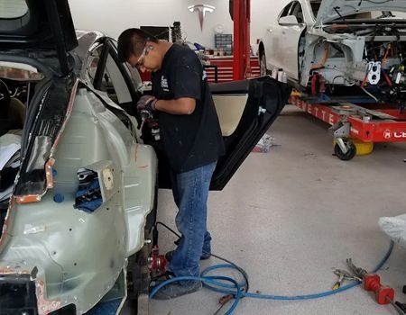 Mechanic working on a car door in a garage, using tools.