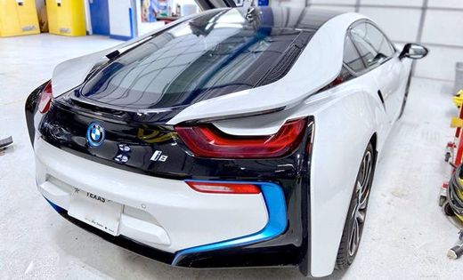 White and black BMW i8 sports car, rear view, in a garage setting. Blue accents.