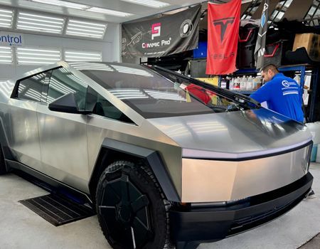 Tesla Cybertruck being cleaned in a shop; worker wiping windshield.