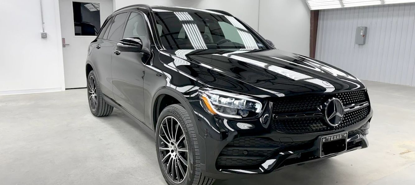 Black Mercedes SUV in a white-walled showroom with multiple light sources, viewed from the front.