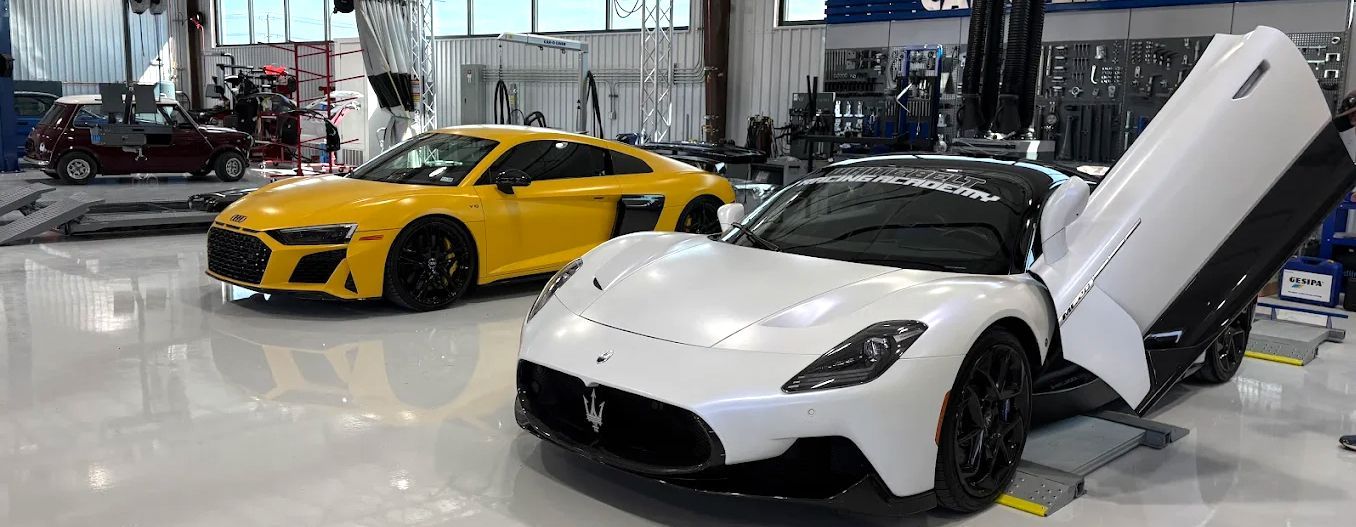 Two sports cars, one yellow and one white with a door open, in a bright garage.