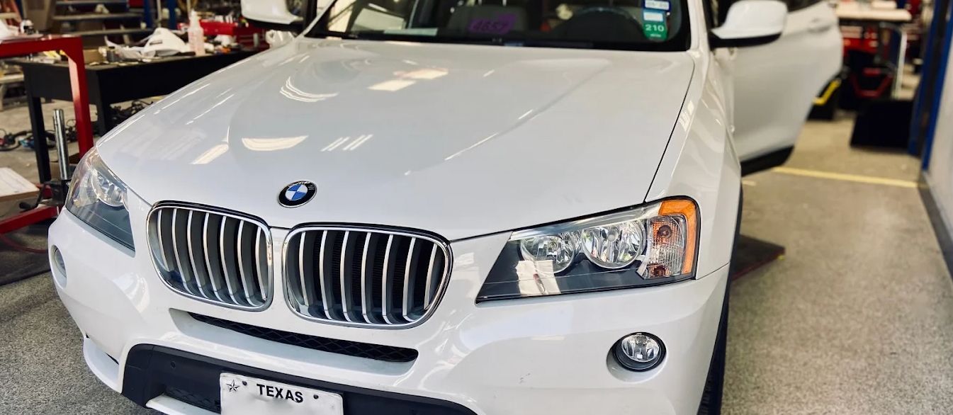 White BMW X3 SUV with an open door in a garage.