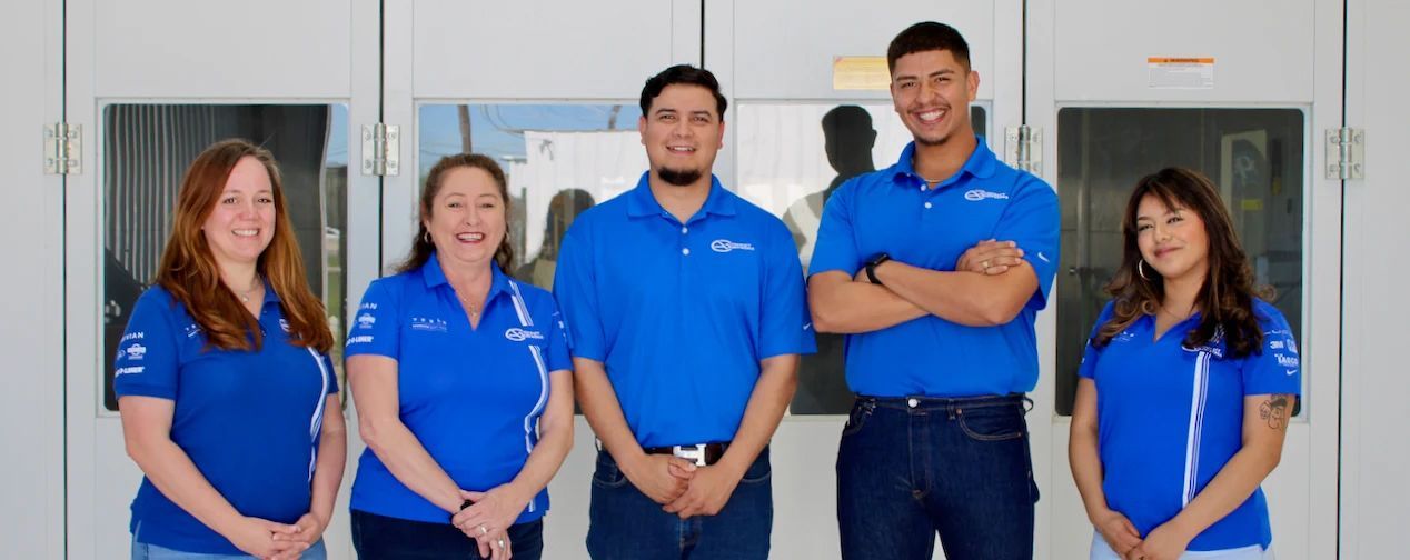 Five people in blue shirts stand in front of a white wall. Two women are on the left, three men on the right.