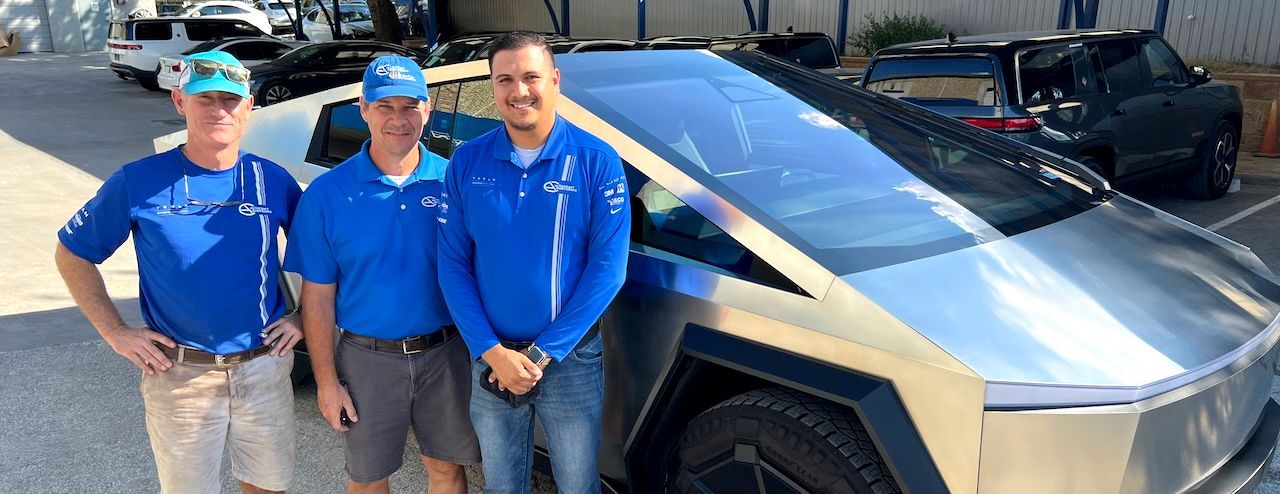 Three people in blue shirts stand next to a silver Tesla Cybertruck.