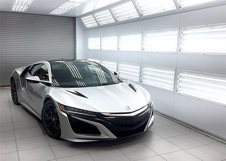 Silver sports car in a brightly lit paint booth.