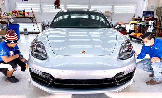 Two people inspecting a silver Porsche Panamera in a garage.