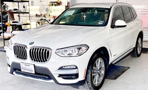White BMW X3 SUV with tinted windows parked indoors. Texas license plate visible.