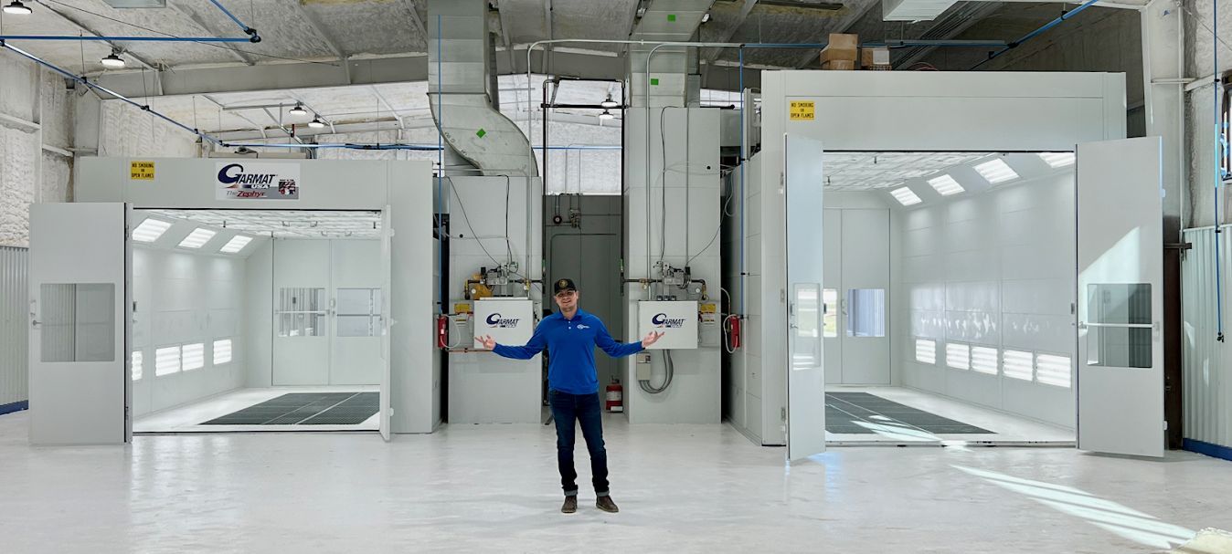 A person standing between two open industrial paint booths in a bright, clean workshop.