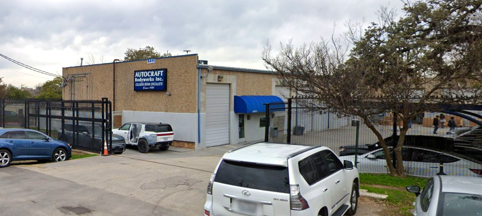 Exterior view of a commercial building with a sign, vehicles parked in front, and a cloudy sky.