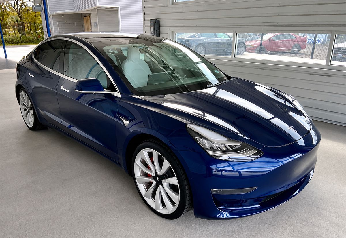 Blue Tesla sedan parked indoors near large windows with a city view