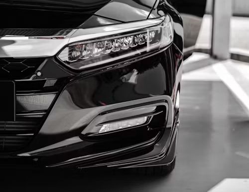 Close-up of a black car’s front headlight and grille in a showroom