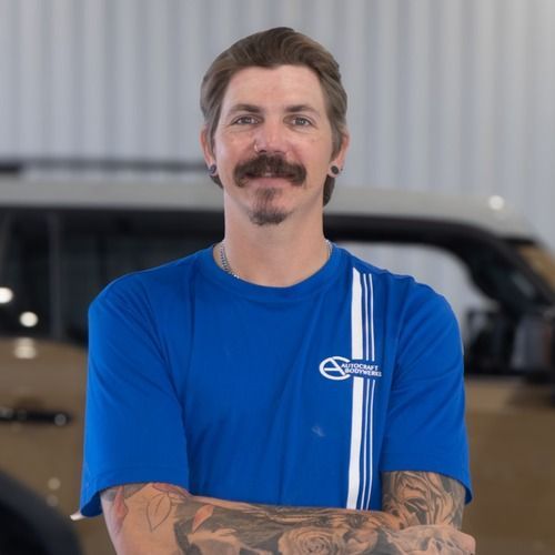 Man in a blue T-shirt with tattooed arms standing indoors in front of a vehicle