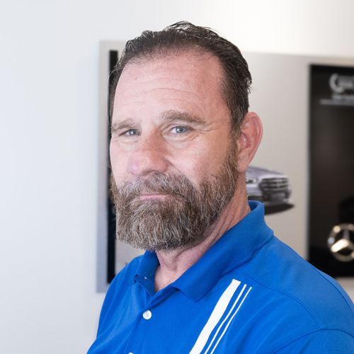 Man in blue polo shirt with beard, standing indoors in front of a car display