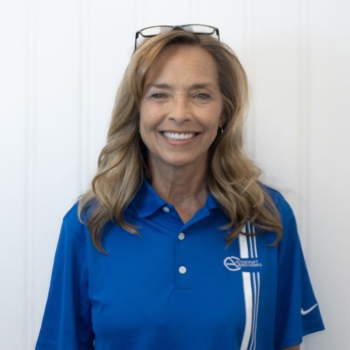 Smiling woman in a blue polo shirt with glasses on her head, standing against a white background