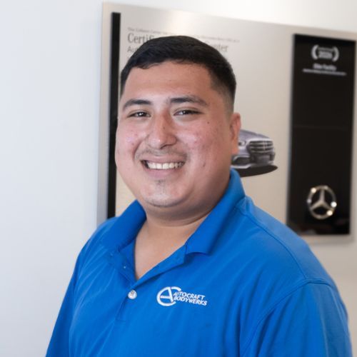 Smiling man in a blue polo shirt standing in a car showroom.